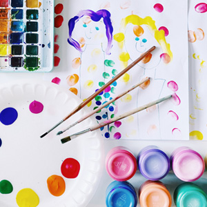 Various colorful paints and brushes with a child's painting of two people