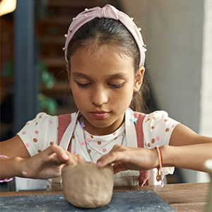 Child molding a clay pinch pot
