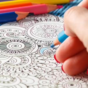 Closeup of hand coloring a floral design with colored pencils