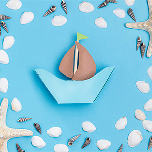 Boat made of craft supplies surrounded by seashells