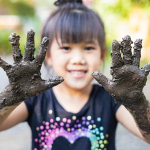 Smiling child holding up muddy hands