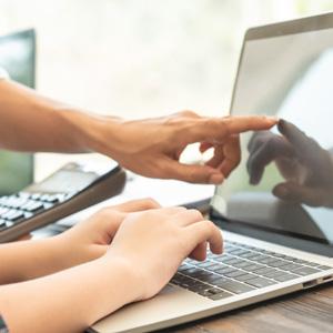 One person rests their hands on a laptop keyboard while another person points at the screen
