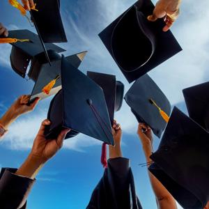 Group of graduates holding mortar board hats up to the sky