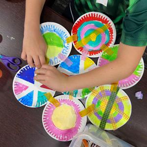Child working on artwork made of painted paper plates and washi tape