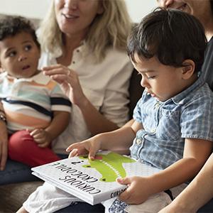 A photo of two children sitting on their caretakers' laps. One child has a board book.