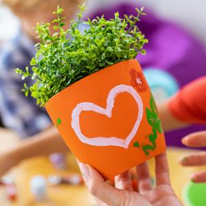 Flower pot painted with a heart and flowers. Blurry kids painting in background.