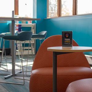 A space with bright blue walls and windows with funky chairs and tall tables