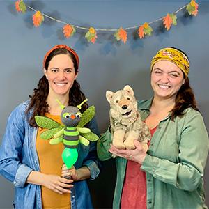 Two smiling women holding puppets, a firefly and a wolf